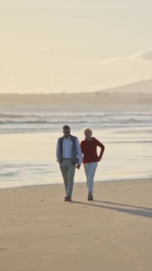 Emekli çift gün batımında sahilde romantik bir yürüyüş yapıyor.