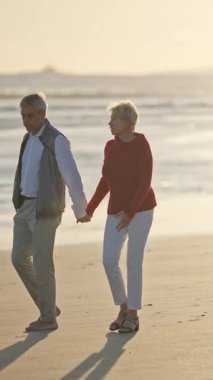 Yaşlı çift gün batımında sahilde romantik bir yürüyüş yapıyor.