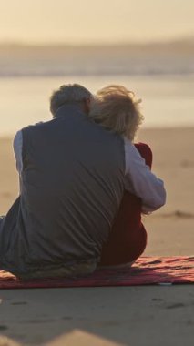 Sevecen, emekli bir çift plaj battaniyesinde huzurlu bir anın tadını çıkarıyor ve okyanusun üzerinde gün batımını seyrediyor.