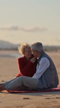 Kıdemli çift gün batımında plaj battaniyesinde samimi anlar paylaşıyor.