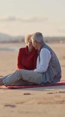 Emekli çift gün batımında plaj battaniyesinde samimi anlar paylaşıyor.