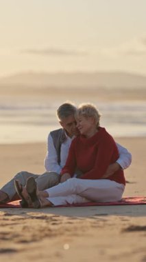 Emekli çift sahilde romantik bir anın tadını çıkarıyor, altın saati kucaklıyor.