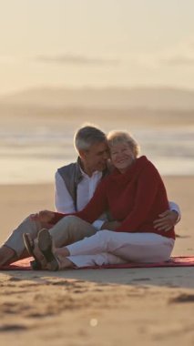 Yaşlı çift gün batımında sahilde romantik bir anın tadını çıkarıyor.