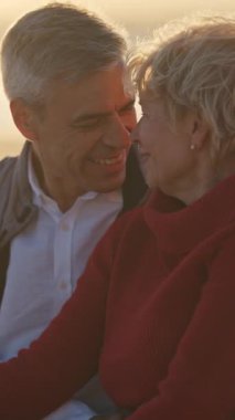 Yaşlı çift gün batımında sahilde romantik bir anın tadını çıkarıyor.