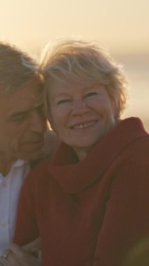 Yaşlı çift gün batımında sahilde romantik bir anın tadını çıkarıyor.