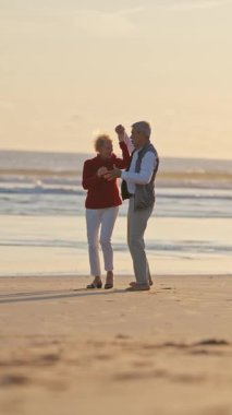 Güzel bir günbatımında kumlu bir sahilde romantik bir dansın tadını çıkaran yaşlı çift.