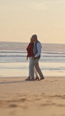 Güzel bir günbatımında kumlu bir sahilde romantik bir dansın tadını çıkaran yaşlı çift.