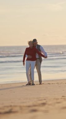 Son sınıf çifti gün batımında sahilde romantik bir yürüyüş yapıyor.