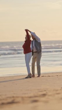Yaşlı çift gün batımında sahilde dans edip sarılıyor.