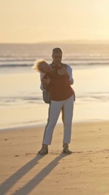 Yaşlı çift gün batımında sahilde romantik bir anın tadını çıkarıyor.