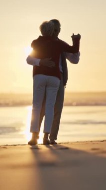 Romantik yaşlı çift, güzel bir altın gün batımında kumsalda dans ediyor.