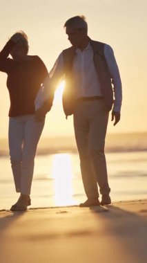 Emekli çift gün batımında sahilde romantik bir yürüyüş yapıyor.