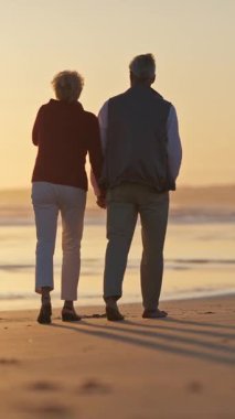 Emekli çift gün batımında sahilde romantik bir yürüyüş yapıyor.