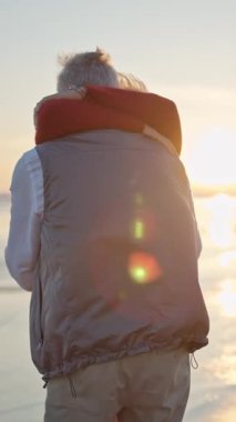 Yaşlı çift romantik bir anın tadını çıkarıyor, güzel bir gün batımında kumsalda sarılıyorlar.