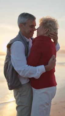 Yaşlı çift gün batımında sahilde romantik bir anın tadını çıkarıyor.