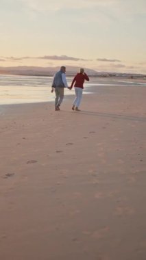 Emekli çift güzel bir gün batımında sahilde romantik bir yürüyüş yapıyor.