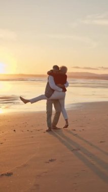 Yaşlı çift sahilde romantik günbatımı yürüyüşünün tadını çıkarıyor.