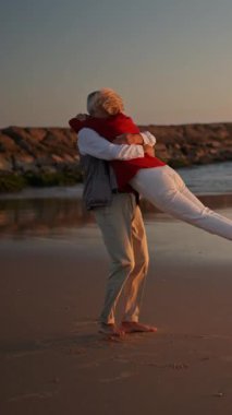 Romantik yaşlı çift güzel bir gün batımında kumsalda hassas bir anın tadını çıkarıyor.