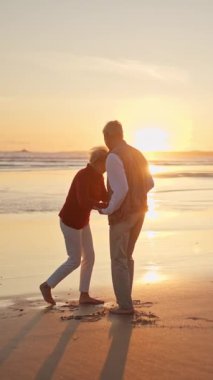 Emekli çift, güzel bir günbatımında sahilde romantik bir dansın tadını çıkarıyor.