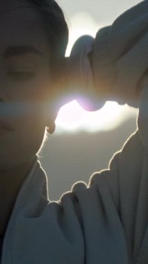 Saçlarını başının arkasında tutan genç bir kadın, günbatımının tadını çıkarıyor.