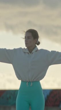 Genç bir kadın zarif bir şekilde dans hareketleri yapıyor kollarını açarak manzaralı bir günbatımı arka planına karşı, sükuneti ve odaklanmayı somutlaştırıyor.