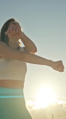 Enerjik bir kadın günbatımında dans ediyor, dinamik hareketler sergiliyor ve neşeli bir ifade sergiliyor.