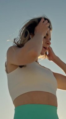 Açık mavi gökyüzünün altında spor giysileri giyen genç bir kadın.