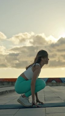 Güzel bir gün batımında binanın çatısında yoga egzersizi yapan beden eğitimi hocası.