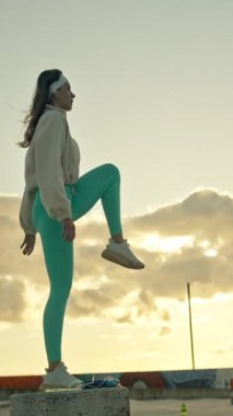 Gün batımında şehir parkında beton bir blokta atlama çalışması yapan kadın sporcu.