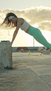 Gün batımında şehir merkezinde beton bir blokta eğik şınav çeken genç bir kadın.