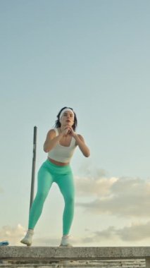 Spor kıyafetleri giyen genç bir kadın beton bir bankta sıçrama yapıyor.