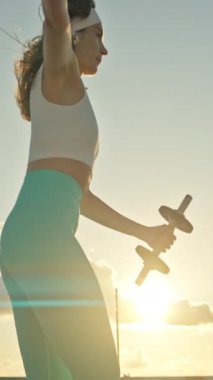 Spor kadını gün batımında dambıllarla hamle yapıyor.