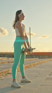 Şehir ortamında günbatımında halterleri kaldıran kadın sporcu.