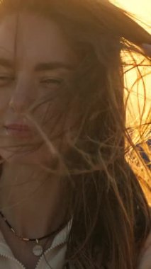 Altın saat gün batımı, kulaklık takan ve saçlarıyla oynayan genç bir kadını aydınlatıyor.