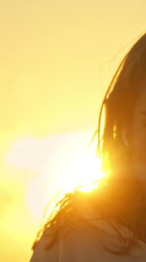 Kapalı gözlü, günbatımının tadını çıkaran dingin genç bir kadının portresi.