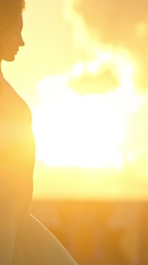 Gün batımında çatıda yoga yapan bir kadının silueti.