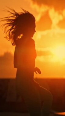 Gün batımında çatıda koşan atletik bir kadının silueti.