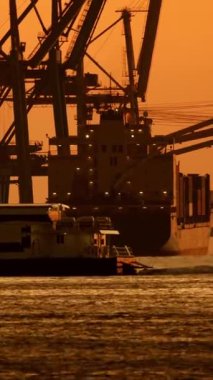 Römorkör, büyük konteynır gemisinin gün batımında ticari limana yanaşmasına yardım ediyor.