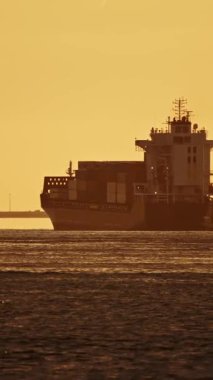 Konteynır gemisi gün batımında köprünün yakınından geçiyor.