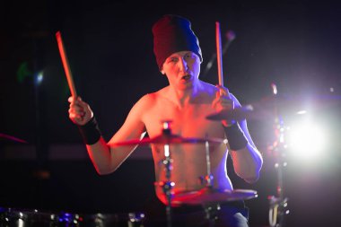 Enerjik davulcu tutkuyla şarkı söylüyor, konser sırasında ritim yaratıyor.