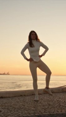 Dansçı, gün doğumunda nehir kenarında zarif pozlar vererek, manzaralı bir şehir zeminine karşı denge ve zarafet sergiliyor.