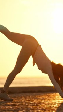 Gün doğumunda üç bacaklı köpek pozu veren genç bir kadın.