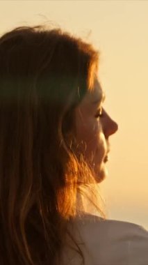 Kulaklıklı sakin kadın deniz kenarında huzurlu bir gün batımının tadını çıkarıyor.