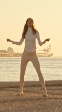 Gün batımında bir iskelede dans eden kadın, altın saatin tadını çıkarıyor.