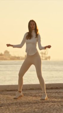 Zarif dansçı günbatımında Tagus nehrinin kenarındaki asfalt bir yüzeyde modern bir dans gösterisi yapıyor.