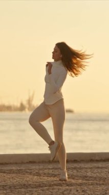 Gün doğumunda arka planda şehir manzarası olan bir iskelede dans eden genç bir kadın.