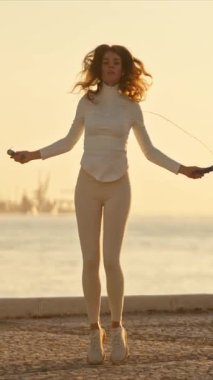 Şafakta deniz kenarında atlama ipiyle egzersiz yapan genç bir kadın.