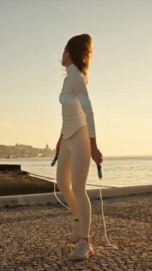 Gün batımında nehir kenarında egzersiz yapan, ip atlayan genç bir kadın.