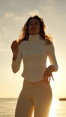 Gün batımında deniz kenarında dans eden genç bir kadın.