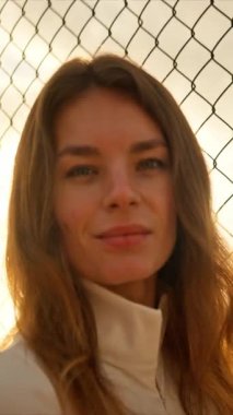 Bir kadın, okyanusa bakan, gün batımının sıcak ışığıyla aydınlatılan zincirli bir çitin yanında dururken huzurlu bir an. Huzurlu ve düşünceli bir ortam.